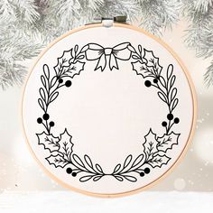 a cross stitch christmas wreath with holly leaves and berries on it, hanging from a tree branch