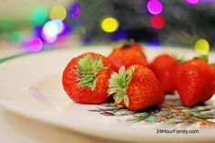 three strawberries sitting on a plate with christmas lights in the backgroung