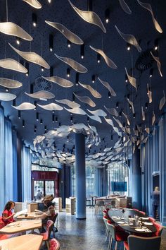 a restaurant with blue walls and ceiling decorated with suspended lights, people sitting at tables