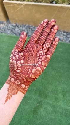 a hand with henna on it is shown in the foreground and green grass behind it