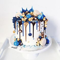 a white and blue cake with chocolate drips on it's top, sitting on a platter