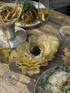 a table topped with plates of food and glasses of wine next to each other on top of a wooden table