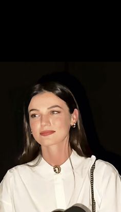 a woman wearing a white shirt and holding a black guitar in her hand, looking at the camera with an intense look on her face