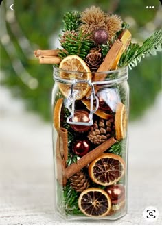 a glass jar filled with cinnamons, orange slices and pine cones sitting on top of a table