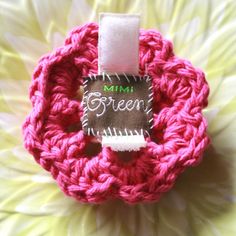 a pink crocheted object with a label on it that says green in front of a white flower