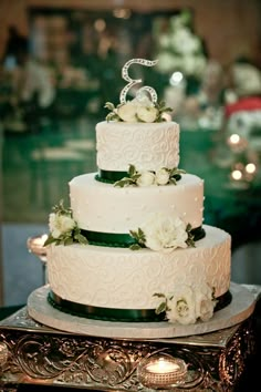 a three tiered wedding cake with white flowers on the top and green ribbon around it