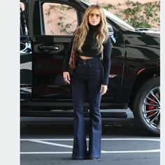 a woman standing in front of a black truck wearing high waisted jeans and heels