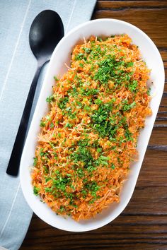 a white dish filled with carrots and parsley on top of a wooden table