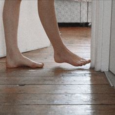 a person's bare feet standing in front of a door on a wooden floor