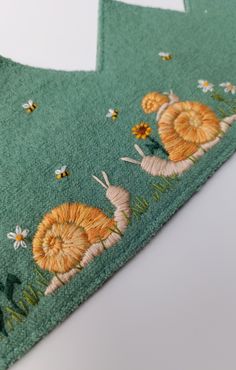 two green aprons with snails and daisies on them, one in the shape of a sunflower