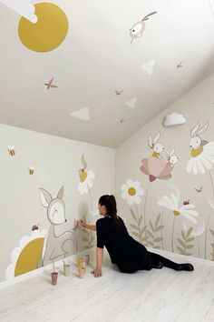 a woman sitting on the floor in front of a wall with flowers and animals painted on it