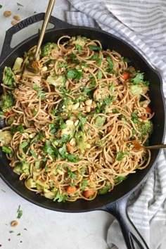 a skillet filled with noodles, broccoli and carrots on top of a table