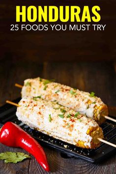 two skewers filled with food sitting on top of a black plate next to a red pepper