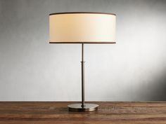 a lamp that is on top of a wooden table next to a gray wall and floor