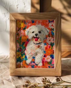 a painting of a small white dog in a wooden frame on a table with flowers