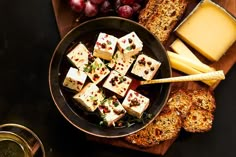 cheese and crackers are on a plate next to bread, grapes, and wine