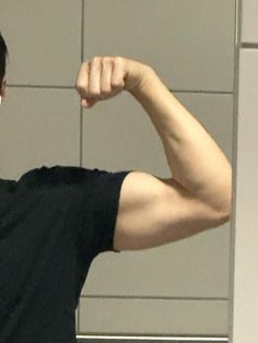 a man flexing his muscles in front of a wall with tiled walls behind him