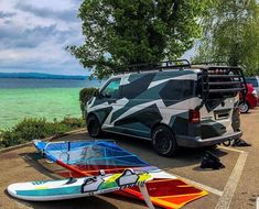 the van is parked next to two surfboards on the side of the road by the water