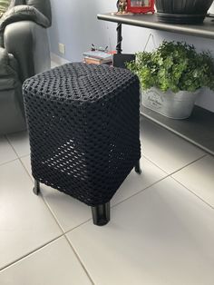 a black stool sitting on top of a white tile floor next to a green plant