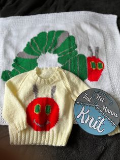 two knitted sweaters are sitting next to each other on a bed with a button