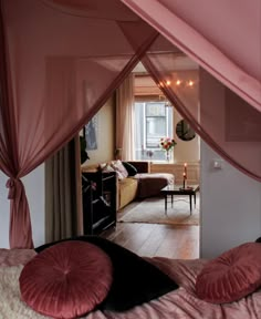 a pink canopy bed in a bedroom next to a living room with a table and chairs