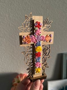 a person holding up a wooden cross with flowers on the front and sides, decorated with crochet