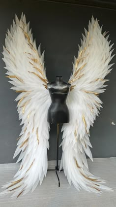 a mannequin head with white and gold wings on it's back stand