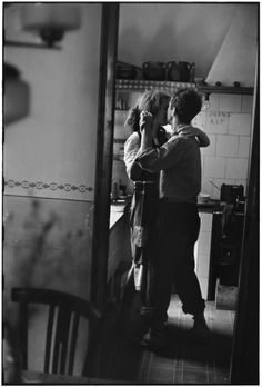 black and white photograph of two people standing in a kitchen, one holding the other's head