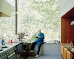 an older man sitting on the counter in a kitchen looking at his cell phone,