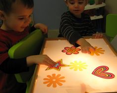 two young boys sitting at a table with paper cut outs on it and one boy holding a lit candle