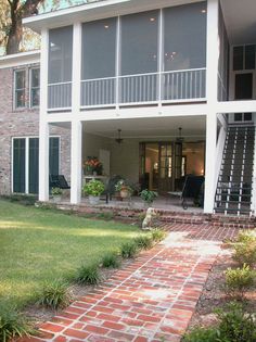 a brick walkway leading to the back of a large house with two balconies