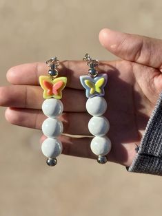 a person is holding two small earrings in their hand, one with a butterfly on it