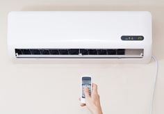 a person holding a remote control in front of a air conditioner with the unit on it's side