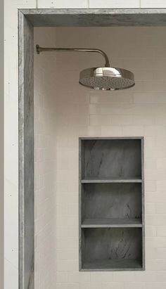 an empty bathroom with white tile walls and shelves on the wall, including a shower head