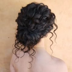 the back of a woman's head with curly hair and no bra, against a beige wall