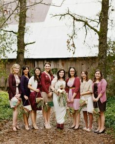 a group of women standing next to each other in front of trees and a barn