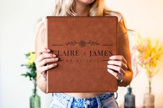 a woman holding up a brown book with the word claire and james on it in front of her face