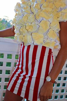 a woman in a red and white striped dress with flowers on her head standing next to a fence