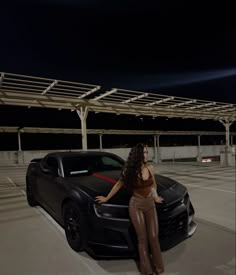 a woman leaning on the hood of a sports car in a parking lot at night