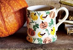 a coffee mug with pumpkins and leaves on it next to a pile of wood