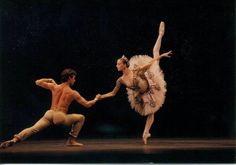 two ballet dancers performing on stage with one holding the other's leg while the other holds his hand