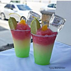 two glasses filled with different colored drinks on top of a table