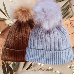 two hats with fur pom - poms on them sitting next to each other