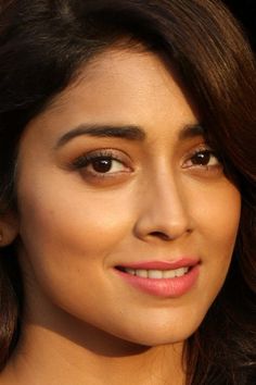 a close up of a woman with brown hair and eyeshadow smiling at the camera