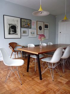 a dining room table with white chairs and pictures on the wall