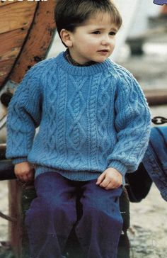 a young boy sitting on top of a wooden bench wearing a blue sweater and pants