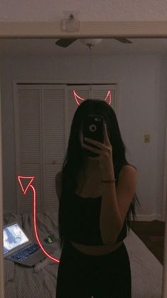 a woman taking a selfie in front of a mirror with devil horns on her head