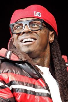 a man with dreadlocks wearing a red hat and glasses, standing in front of a crowd