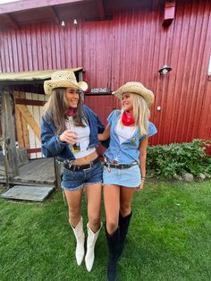 two women wearing cowboy hats and jeans are standing in the grass near a red barn