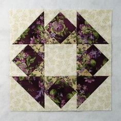 a quilted square with purple flowers and green leaves on the top, in front of a white background